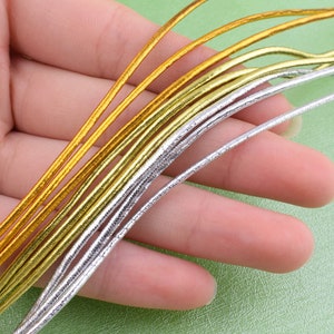 May include: A close-up of a bundle of gold and silver elastic cord. The cord is thin and has a metallic sheen.
