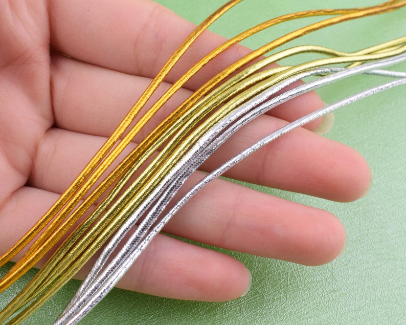 May include: A close-up of a bundle of gold and silver elastic cord. The cord is thin and has a metallic sheen.