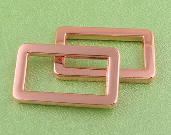 Puede incluir: Dos bucles rectangulares de metal dorado rosa para hebilla de cinturón. Los bucles están apilados uno encima del otro.