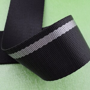 May include: Black webbing with a reflective silver stripe. The webbing is woven and has a textured surface.