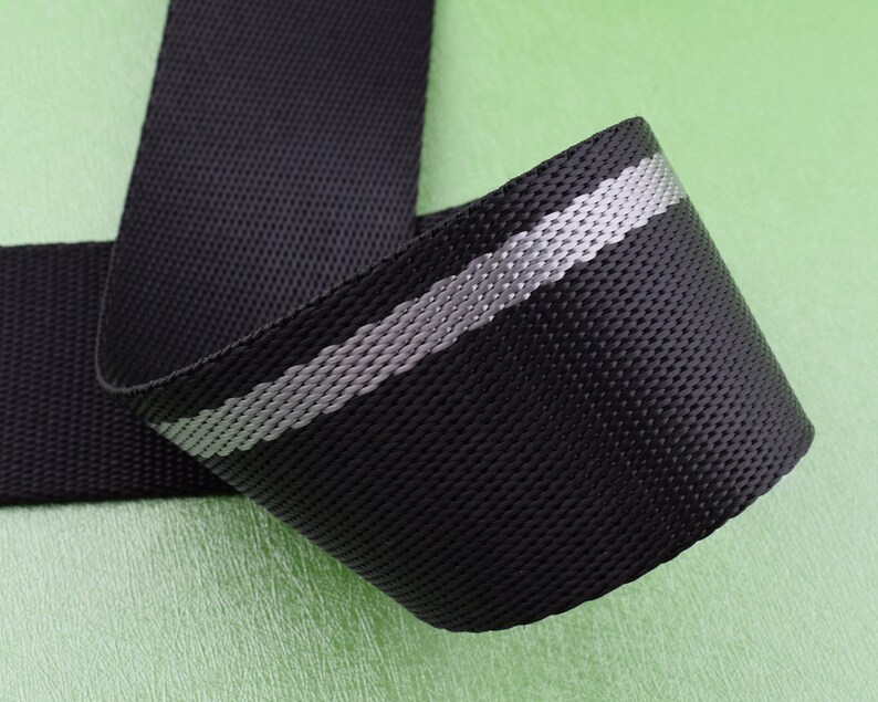 May include: Black webbing with a reflective silver stripe. The webbing is woven and has a textured surface.