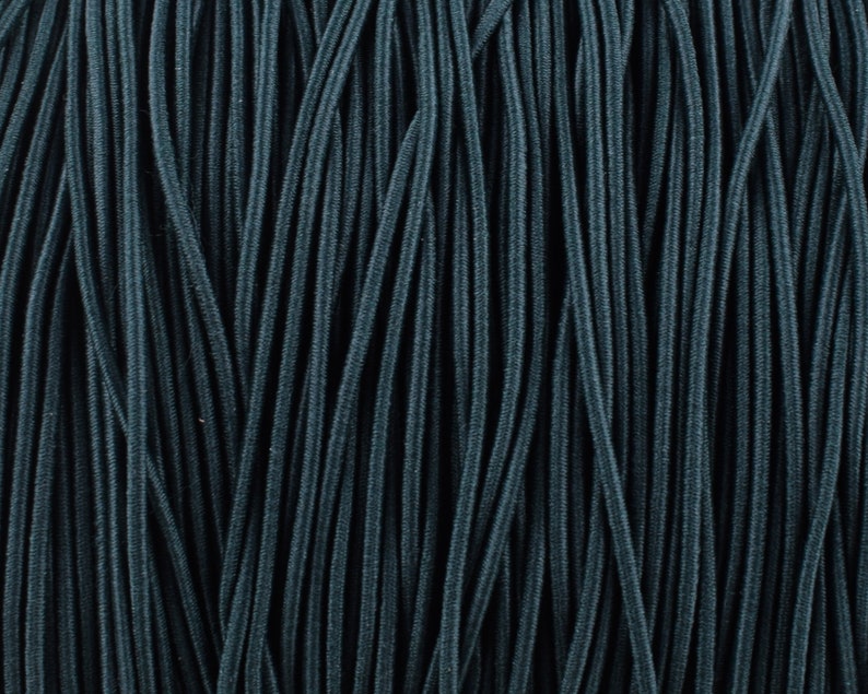 May include: Close-up of a bundle of dark teal elastic cord. The cord is arranged in parallel lines, creating a textured background.