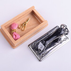 May include: A miniature sewing machine with a black metal body and a silver base. A wooden box with a pink thread spool and gold scissors is also included.