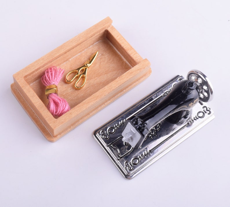 May include: A miniature sewing machine with a black metal body and a silver base. A wooden box with a pink thread spool and gold scissors is also included.