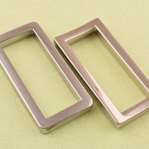 May include: Two silver metal rectangular belt buckle loops. The loops are smooth and shiny.