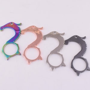 May include: Four different colored metal keychains shaped like a seahorse. The keychains have a loop on the top and a small ring on the bottom. The colors are rainbow, rose gold, silver, and black.