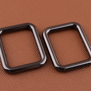 May include: Two black metal D-rings, each with a square shape and a smooth, polished finish.