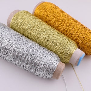 May include: Three spools of metallic thread, one silver, one gold, and one a lighter shade of gold. The spools are wound with thread and have cardboard cores.