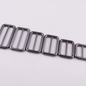 May include: A set of six black metal slider buckles in various sizes. The buckles are rectangular with a smooth finish and two parallel bars across the center.