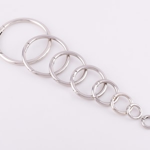 May include: A set of seven silver-toned metal key rings of varying sizes. The key rings are all open and have a spring-loaded clasp.