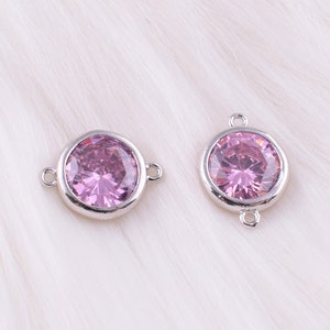 May include: Two silver-toned connector charms with a round, faceted pink crystal in the center. Each charm has two loops for attaching to jewelry.
