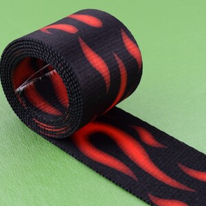 Puede incluir: Cinta negra y roja con un patrón de llamas. La cinta está enrollada y el patrón de llamas es visible tanto en la parte enrollada como en la parte desenrollada.