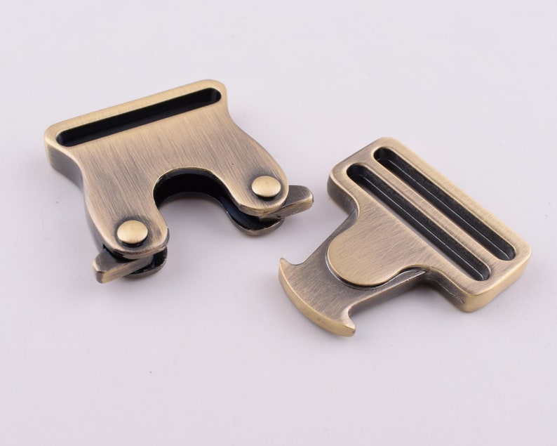 May include: Two antique gold metal clasps with black accents. The clasps are designed to be used for attaching straps or belts.
