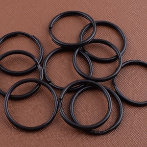 Puede incluir: Un montón de llaveros de metal negro. Los anillos son de diferentes tamaños y están dispuestos en un patrón aleatorio.