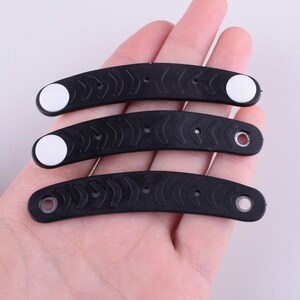 Puede incluir: Tres gomas para el pelo de pl&aacute;stico negro con detalles blancos. Las gomas para el pelo son curvadas y tienen una superficie texturizada.
