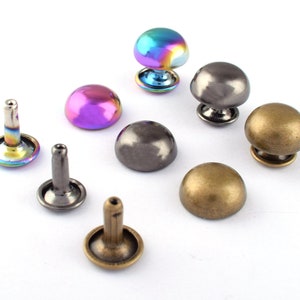 May include: Assortment of metal dome-shaped studs in various finishes, including gold, silver, and iridescent. The studs have a flat base and a raised dome top.