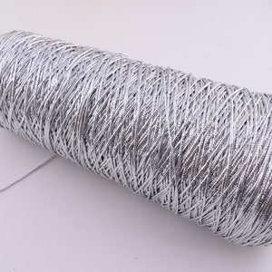 May include: A spool of silver metallic thread. The thread is wound tightly around the spool, creating a textured surface.