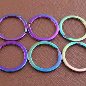 May include: Six iridescent key rings in a rainbow color scheme. The key rings are made of metal and are all the same size.