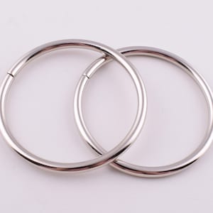 Op de afbeelding: Twee zilveren metalen ringen, waarvan er één iets groter is dan de andere, zijn in elkaar gehaakt. De ringen zijn glad en hebben een gepolijste afwerking.