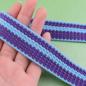 May include: Purple and light blue striped woven ribbon. The ribbon is woven with a textured pattern.