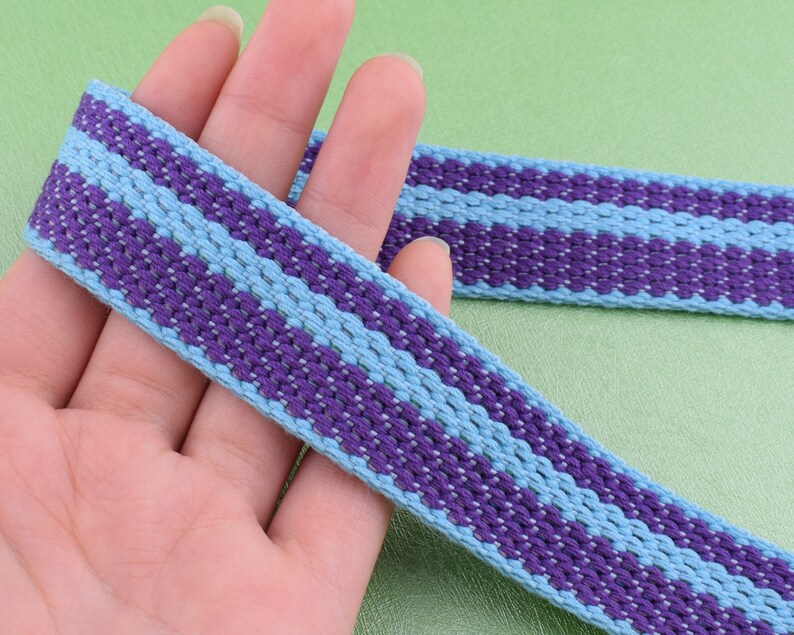 May include: Purple and light blue striped woven ribbon. The ribbon is woven with a textured pattern.
