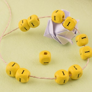Puede incluir: Una cuerda de cuentas de madera amarillas con la letra "I" impresa en cada cuenta. Las cuentas están enhebradas en una cuerda de hilo natural.