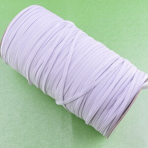 May include: A roll of white elastic string wound around a cardboard tube. The elastic is a light gray color and is tightly wound.