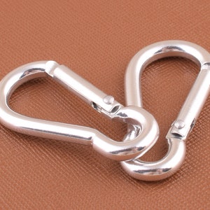 May include: Two silver metal carabiners linked together. The carabiners are a common type of clip used for attaching items to a backpack or other gear.