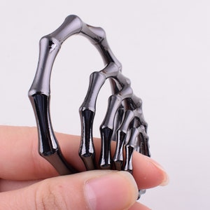 May include: A set of five black metal rings, each shaped like a hand with fingers, are stacked on top of each other. The rings are connected to each other, forming a chain.