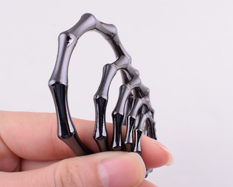 May include: A set of five black metal rings, each shaped like a hand with fingers, are stacked on top of each other. The rings are connected to each other, forming a chain.