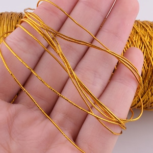 May include: A spool of gold metallic cord, with a few strands of the cord wrapped around a hand.