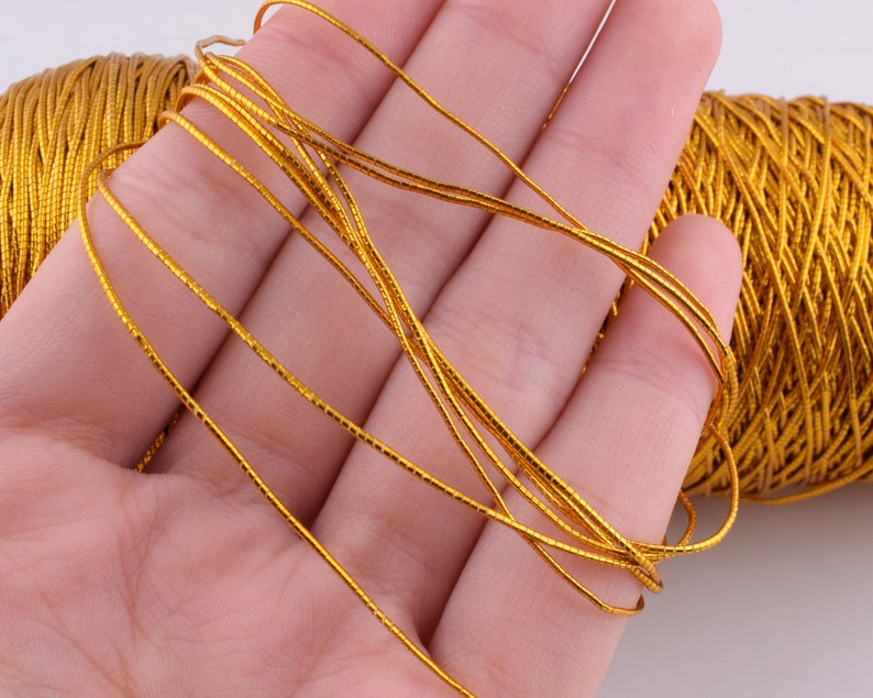 May include: A spool of gold metallic cord, with a few strands of the cord wrapped around a hand.