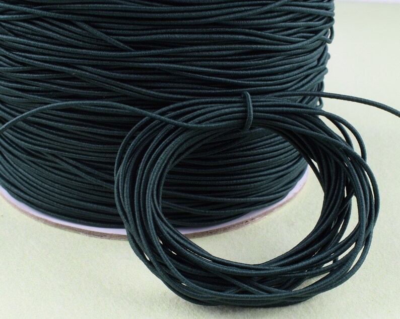 May include: A spool of dark green elastic cord. The cord is wound tightly around the spool and is ready to be used for crafting projects.