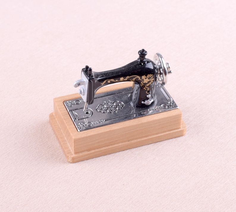 May include: A miniature black sewing machine with gold accents and a wooden base. The machine has a decorative floral design and a silver needle.