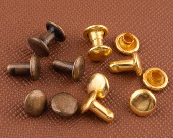 May include: Assortment of gold and bronze metal rivets with a round head and a post. The rivets are on a brown leather surface.