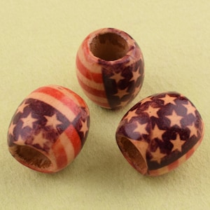 May include: Three wooden beads with a red, white, and blue American flag design. The beads are oval shaped and have a hole in the center.