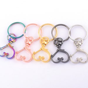 Peut inclure: Cinq mousquetons pivotants en métal avec des porte-clés de différentes couleurs : irisé, or rose, or, canon de fusil et argent. Chaque fermoir a un design en forme de cœur. Les porte-clés sont ronds et assortis à la couleur du fermoir.