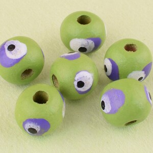 May include: Six green wooden beads with purple and white painted eyes. The beads have a hole through the center for stringing.