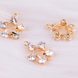 May include: Three gold-tone metal charms with clear crystal accents. Each charm features a star-shaped design with a circular center.