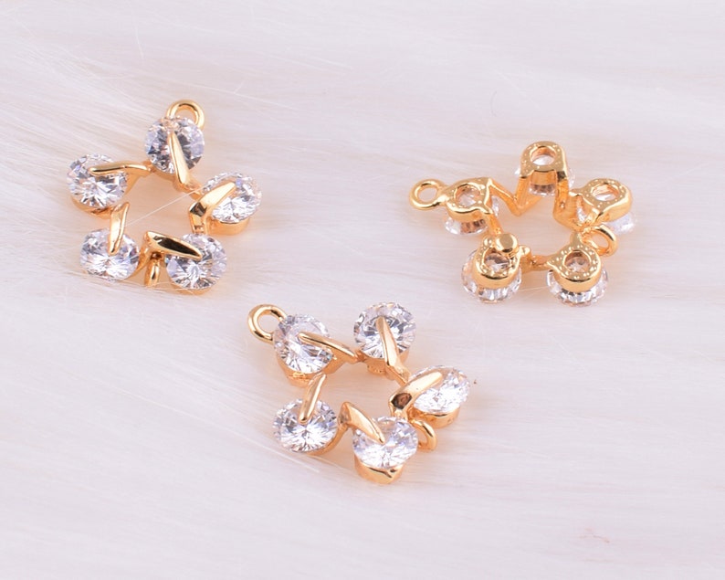 May include: Three gold-tone metal charms with clear crystal accents. Each charm features a star-shaped design with a circular center.