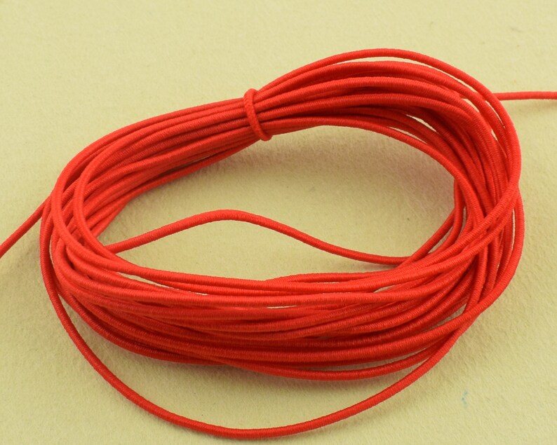 May include: A coil of bright red elastic cord, tightly wound and knotted. The cord is smooth and appears to be made of a synthetic material. The background is a light beige color.