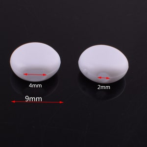 May include: Two white plastic beads, one measuring 9mm in diameter and 4mm in height, and the other measuring 2mm in height.