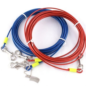 Puede incluir: Dos cables de sujeción para perros, uno azul y otro rojo, enrollados sobre una superficie blanca. Cada cable tiene un clip metálico y un protector de plástico amarillo. Un pequeño peine metálico está unido a uno de los cables.