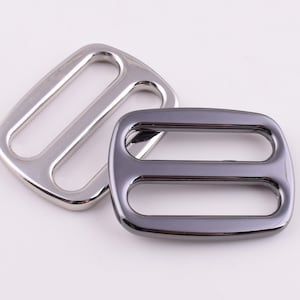 May include: Two metal slider buckles, one silver and one black. Both buckles have two parallel slots.