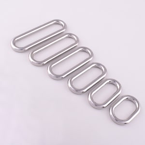 Könnte beinhalten: Ein Satz von sieben silbernen ovalen Metallringen in verschiedenen Größen. Die Ringe sind in absteigender Größenordnung von links nach rechts angeordnet.