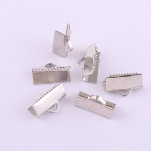 Puede incluir: Seis terminales de cordón de metal plateado con un borde decorativo. Los terminales tienen un pequeño bucle en el lateral.