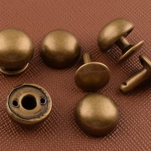 Puede incluir: Surtido de remaches y tachuelas de metal de color dorado antiguo. Algunos tienen una parte superior abovedada, mientras que otros tienen una parte superior plana con un agujero en el centro. Son ideales para la elaboración de cuero, proyectos de bricolaje y para agregar un toque vintage a tus creaciones.