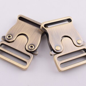 May include: Two antique gold metal buckle closures with a double-loop design. The buckles are made of metal and have a brushed finish.