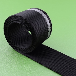 May include: Black webbing with a reflective silver stripe. The webbing is rolled up and the reflective stripe is visible.