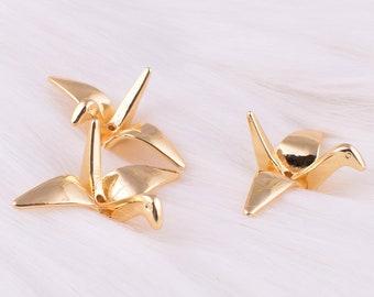 Könnte beinhalten: Drei goldene Origami-Kranich-Anhänger. Die Kraniche sind im traditionellen Stil gefaltet und haben oben ein Loch zum Aufhängen.